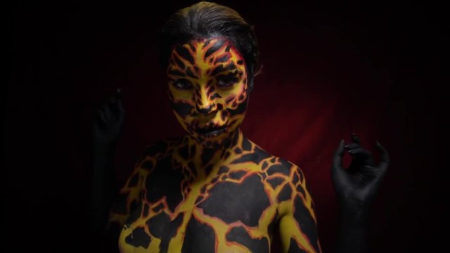 A girl with a bodypainting on her body in the form of volcanic lava, which breaks out of the ground slowly moves her body, slow motion