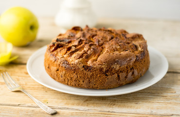 HOMEMADE RUSTIC APPLE CAKE PIE POWDERED WITH SUGAR ON A WHITE PLATE ON A WOODEN TABLE