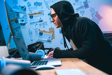 serious hooded hacker working with computer to develop malware