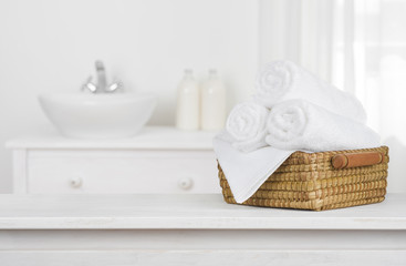 Fototapeta na wymiar Towels basket on wooden table top with blurred bathroom interior