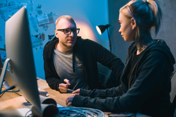 couple of hackers chatting at workplace in dark room