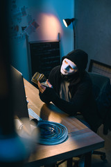 hacker in mask counting stolen money at his workplace