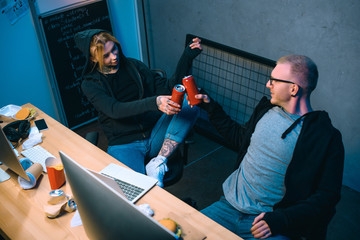 high angle view of couple of hackers clinking cans of beer at workplace