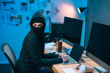 female hacker in mask developing malware at workplace