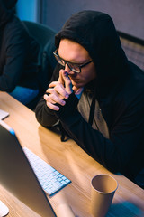 thoughtful hooded hacker looking at computer screen