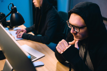 thoughtful young hacker looking at computer screen in dark room