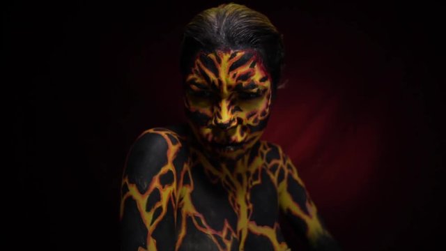 A girl with a bodypainting on her body in the form of a volcanic lava looks discontentedly and raises her black hand