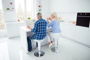 Fototapeta na wymiar Full size, fullbody rear view portrait of sweet attractive lovely stylish couple sitting at the table in kitchen, man reading magazine, woman having mug of tea, enjoying morning time together