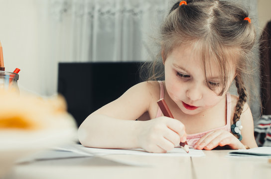 Cute little girl draws with colored pencils at home