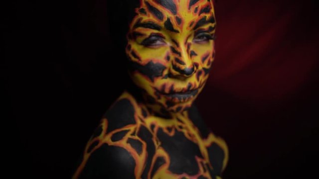 A girl with a bodypainting on her body in the image of a volcanic lava looks at her friend with displeasure