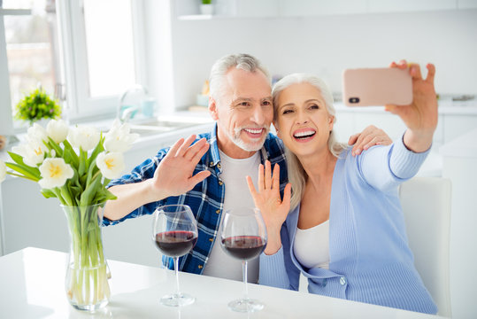 Portrait of lovely attractive stylish cheerful couple drinking red wine alcohol, shooting selfie on front camera, using smart phone, embracing, hugging, gesturing hello symbol, sign with palm