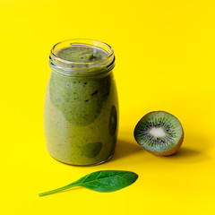 Green smoothie with kiwi and leaf of spinach on yellow background