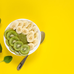 Green smoothie in a white bowl on yellow background
