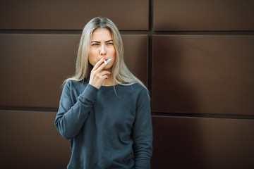 A young pretty girl smokes a cigarette in the street in the spring.