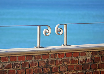 brick wall with wrought iron handrail. On background the blue sea