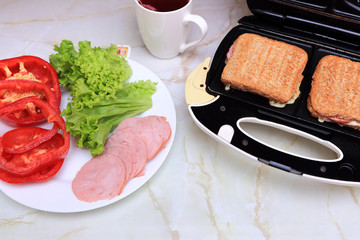 Posiłek z tostów robionych w tosterze, sałaty, papryki, kiełbasy szynkowej i herbaty owocowej.