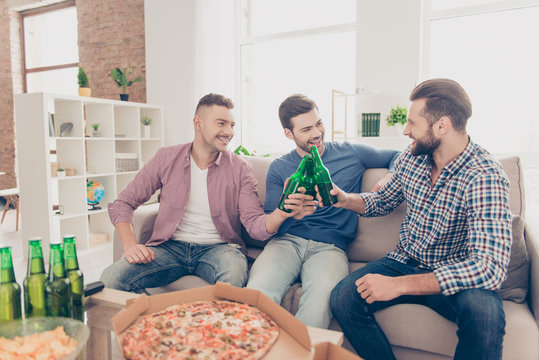 Attractive, stylish, modern, cheerful, trendy guys embracing having, clinking bottle with lager for soccer word cup, speaking, talking, sitting in living room, spending time, holiday together