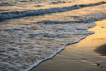 Waves approaching sandy beach during sunset