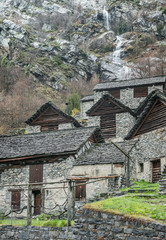 Fototapeta na wymiar traditional alpine village with many small wooden and stone houses and a mountain waterfall backdrop