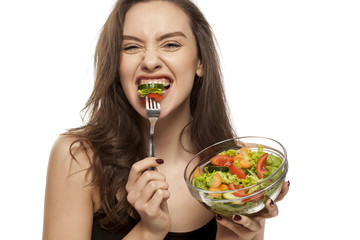 Young beautiful woman eating salad on white background