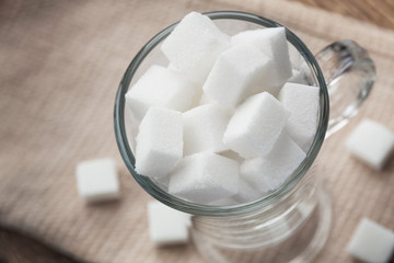Cubes of white sugar in a glass cup on a background of a beige towel. Closeup, selective focus, top view