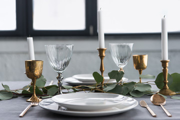 close up view of rustic table setting with wine glasses, eucalyptus, vintage cutlery, candles in candle holders and empty plates - Powered by Adobe