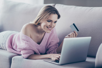 Fototapeta na wymiar Buyer people person concept. Portrait of excited beautiful cheerful pretty attractive lady holding credit card in hand searching doing shopping online lying on comfortable divan using netbook