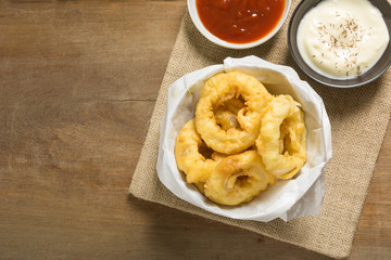 top view of crunchy fried onion rings served with ketchup and mayonnaise on wooden table, copy space. homemade style snack concept.