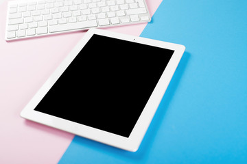 Computer keyboard next to tablet on pink and blue background. Technology.