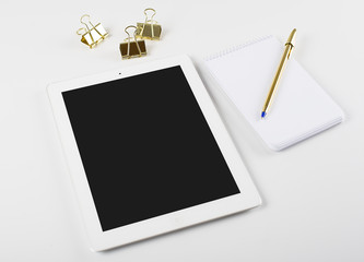 Tablet and notebook next to ballpoint pen and golden clips on white background.