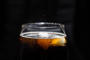 A glass of cola beverage with a salt. On a black background.