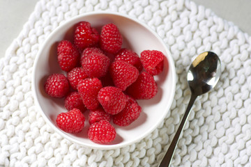 white cup of fresh raspberries on cotton white placemat
