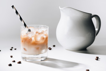 close up view of jag of milk and glass of cold brewed coffee with straw on white tabletop