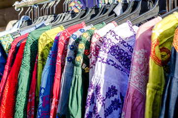 Hangers with different fashion stylish female clothes on clothing rack women handmade embroidery dresses sale concept colorful selection of t-shirts ultra violet, pink, blue, white, yellow,