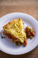 Classic homemade shepherd's pie (mashed potato and ground beef with vegetables) in white plate on wooden table. overhead, horizontal
