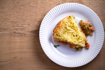 Classic homemade shepherd's pie (mashed potato and ground beef with vegetables) in white plate on wooden table. horizontal