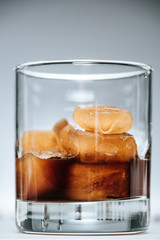 close up view of cold iced coffee with ice cubes in glass on grey background