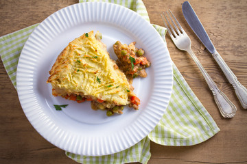 Classic homemade shepherd's pie (mashed potato and ground beef with vegetables) in white plate on wooden table. horizontal