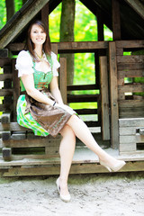 young woman wearing a dirndl sitting at wooden lodge