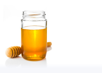 Golden yellow heney in clear glass jar with wood honey dipper on its side, all on white background