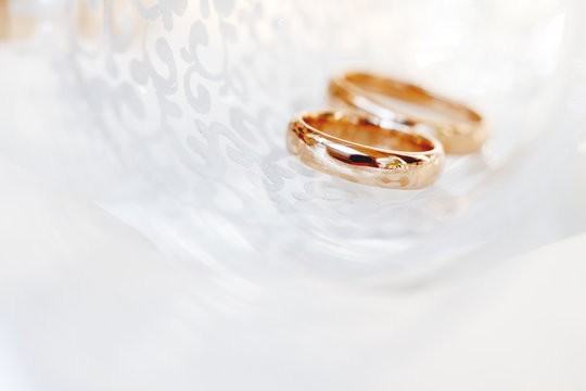 Wedding golden rings in transparent glass. Symbol of love and marriage. Creative picture with glass glittering in the sunlight.