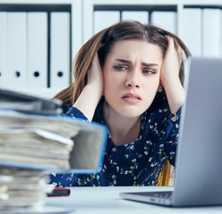 Tired and exhausted woman looks at the mountain of documents propping up her head with her hands.