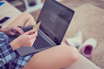 Woman's hands holding a credit card and using laptop for online shopping. Girl shopping online sitting on the couch at home.