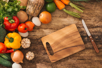 Fresh vegetables around cutting board on rustic background. Top view, healthy cooking concept.