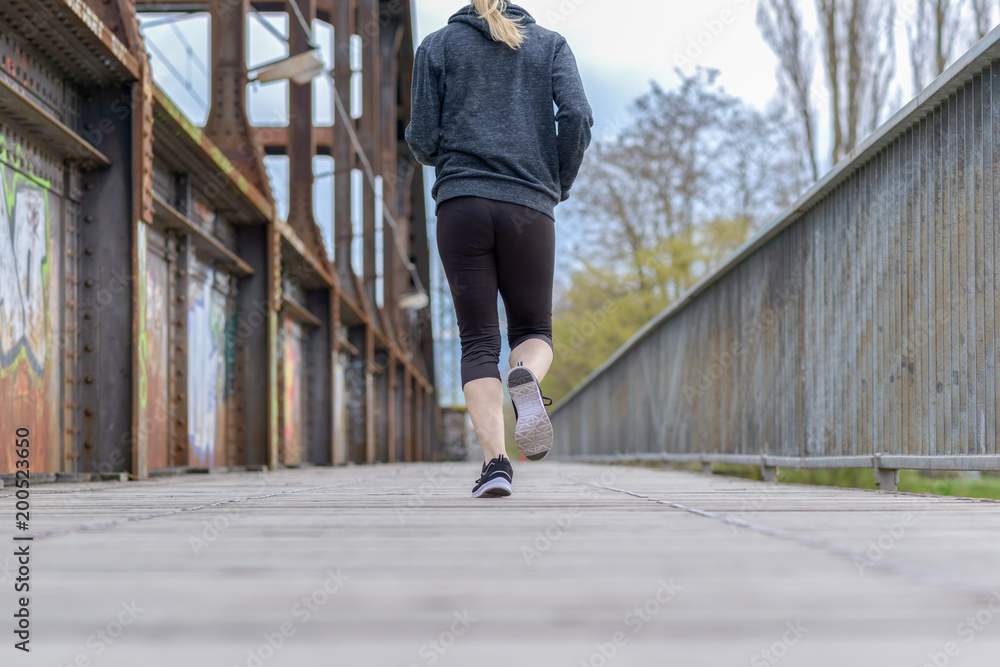 Poster Sporty woman running on an old boardwalk bridge