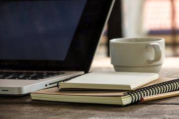 Top view of blank notebook with white coffee, laptop and with natural light on wooden table.