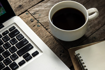 Top view of blank notebook with white coffee, laptop and with natural light on wooden table.