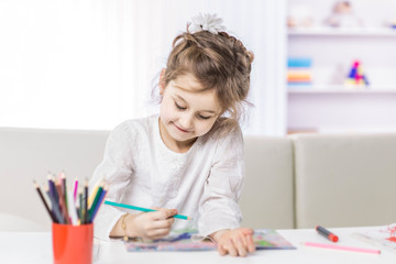 five year old girl draws with crayons sitting at table in the nursery