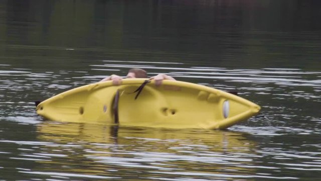 A man flips over his already tipped kayak while he is in the water.