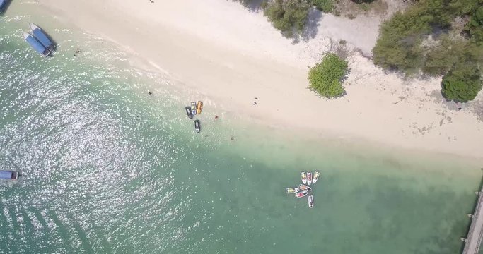 Boats and tourists on the white sand shores of a tropical island. Birds eye view.
